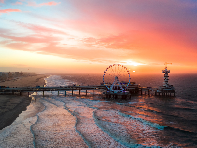 Strand von Scheveningen aus der Vogelperspektive mit Pier, Riesenrad und Leuchtturm bei Sonnenuntergang