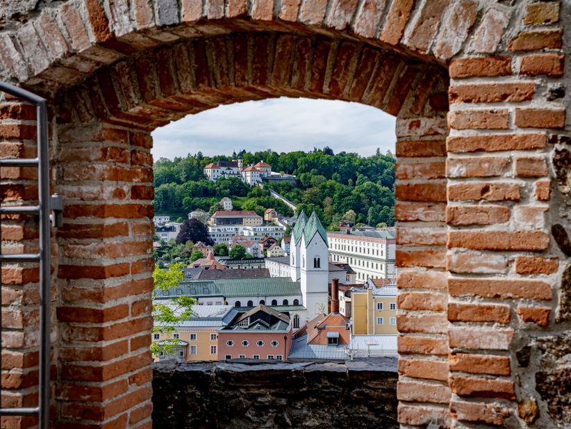 Durch eine gemauerte Toröffnung fällt der Blick auf Passau in Deutschland mit der Wallfahrtskirche und dem Paulinerkloster.