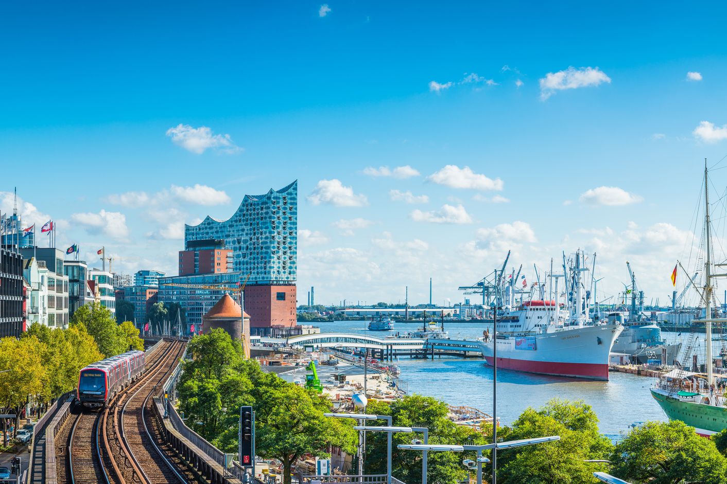 Hamburger Hafen mit Schiffen, einer Bahn und der Elbphilharmonie bei blauem Himmel