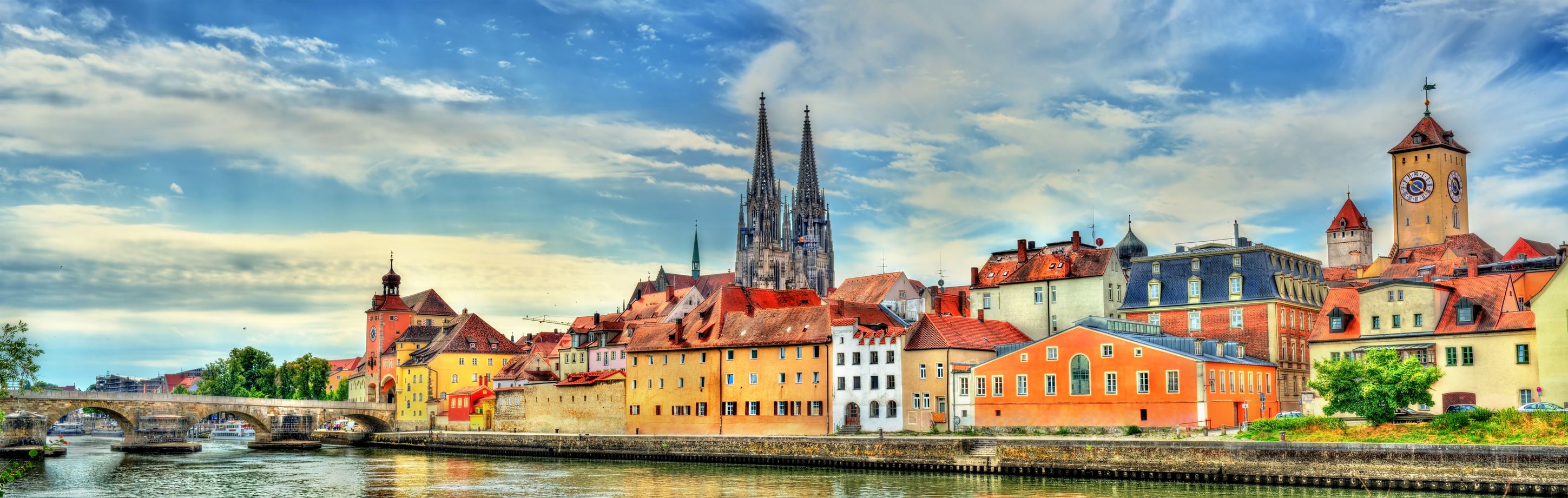 Blick vom Wasser auf die Steinerne Brücke und die Altstadt von Regensburg mit blauem Himmel.