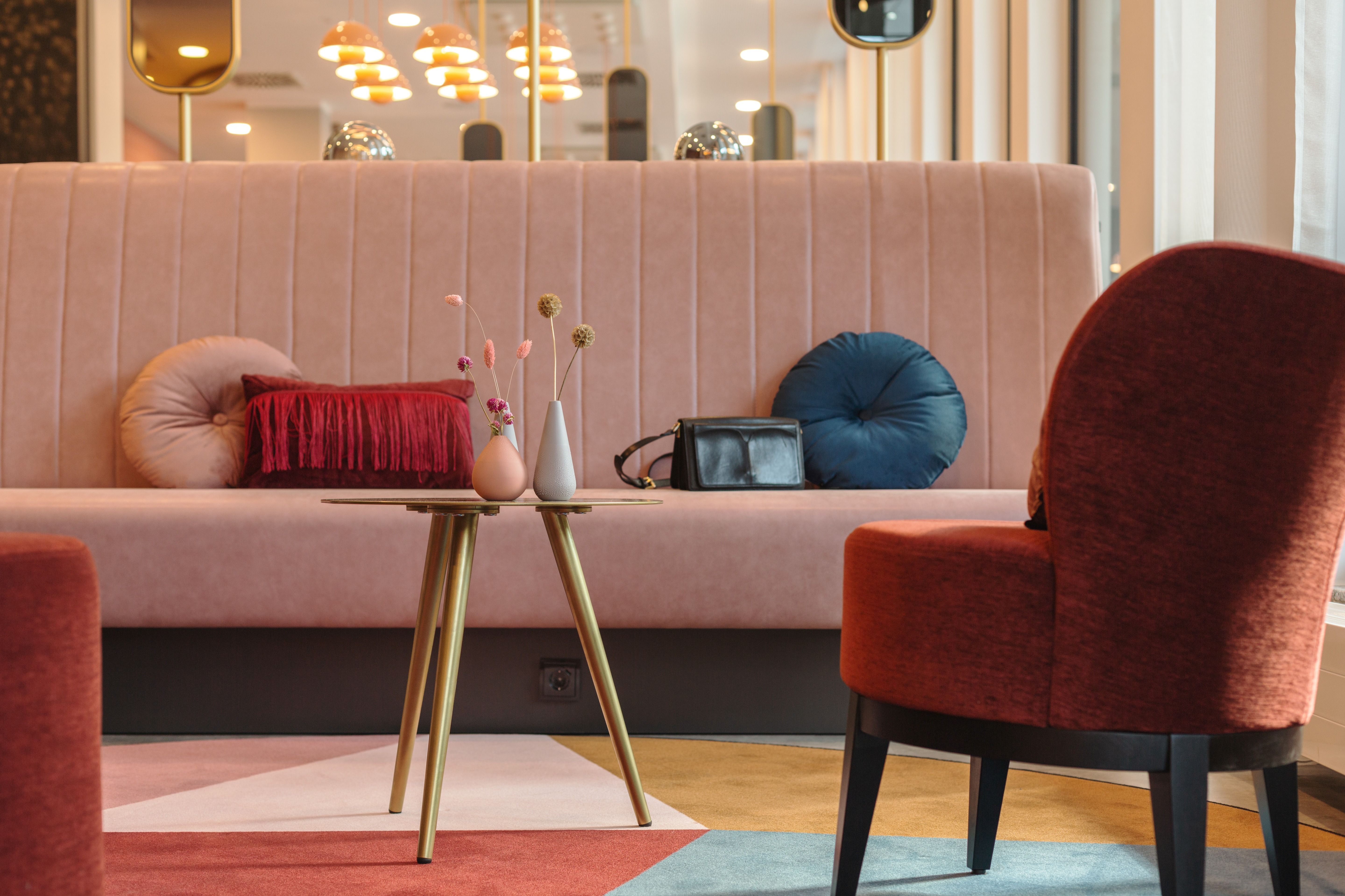 Modernes Hotel-Foyer mit einem roten Sessel, einem cremefarbenen Sofa und einem Holztisch.