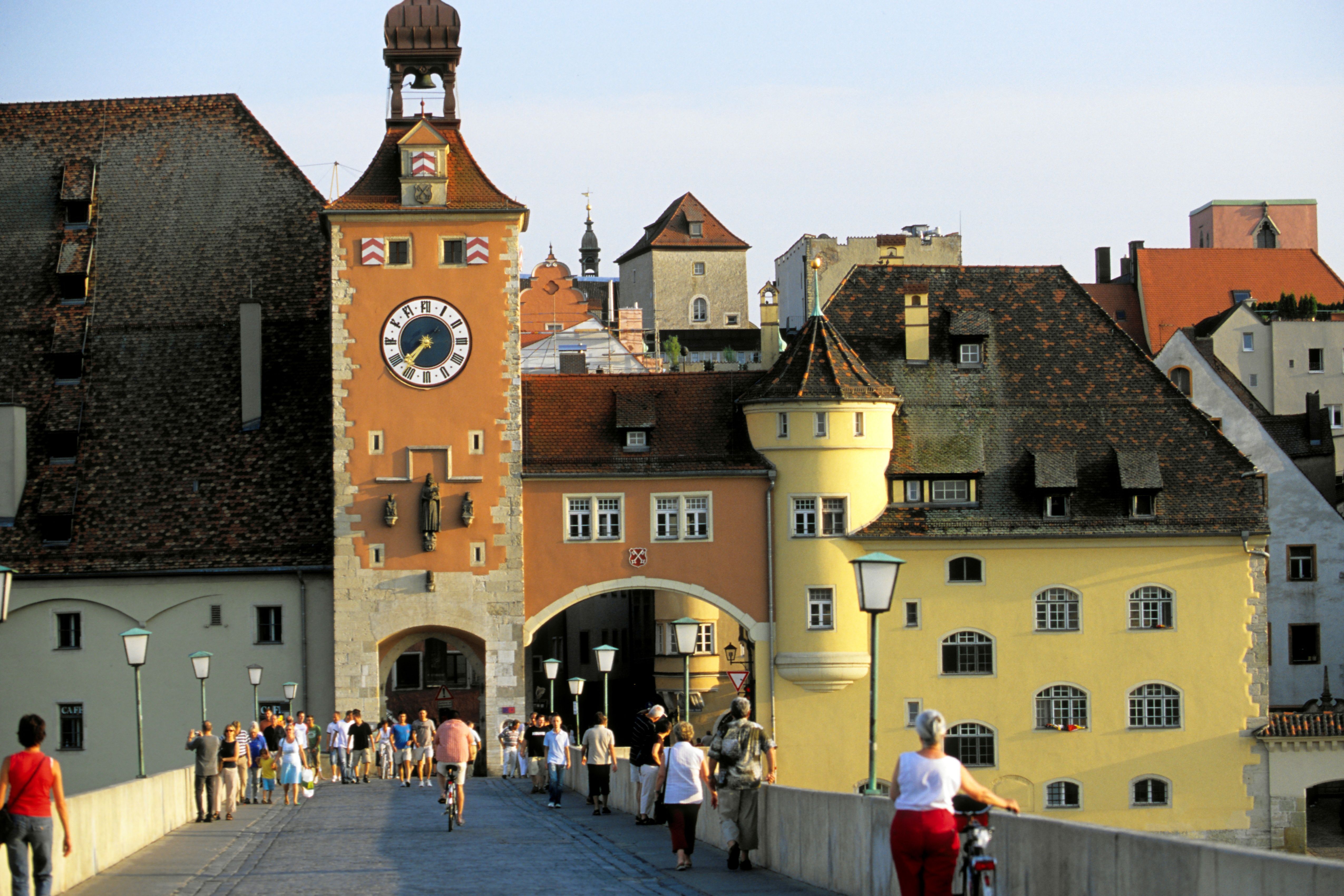 Die Steinerne Brücke in Regensburg mit Menschen, die bei sonnigem Wetter über das historische Bauwerk spazieren.