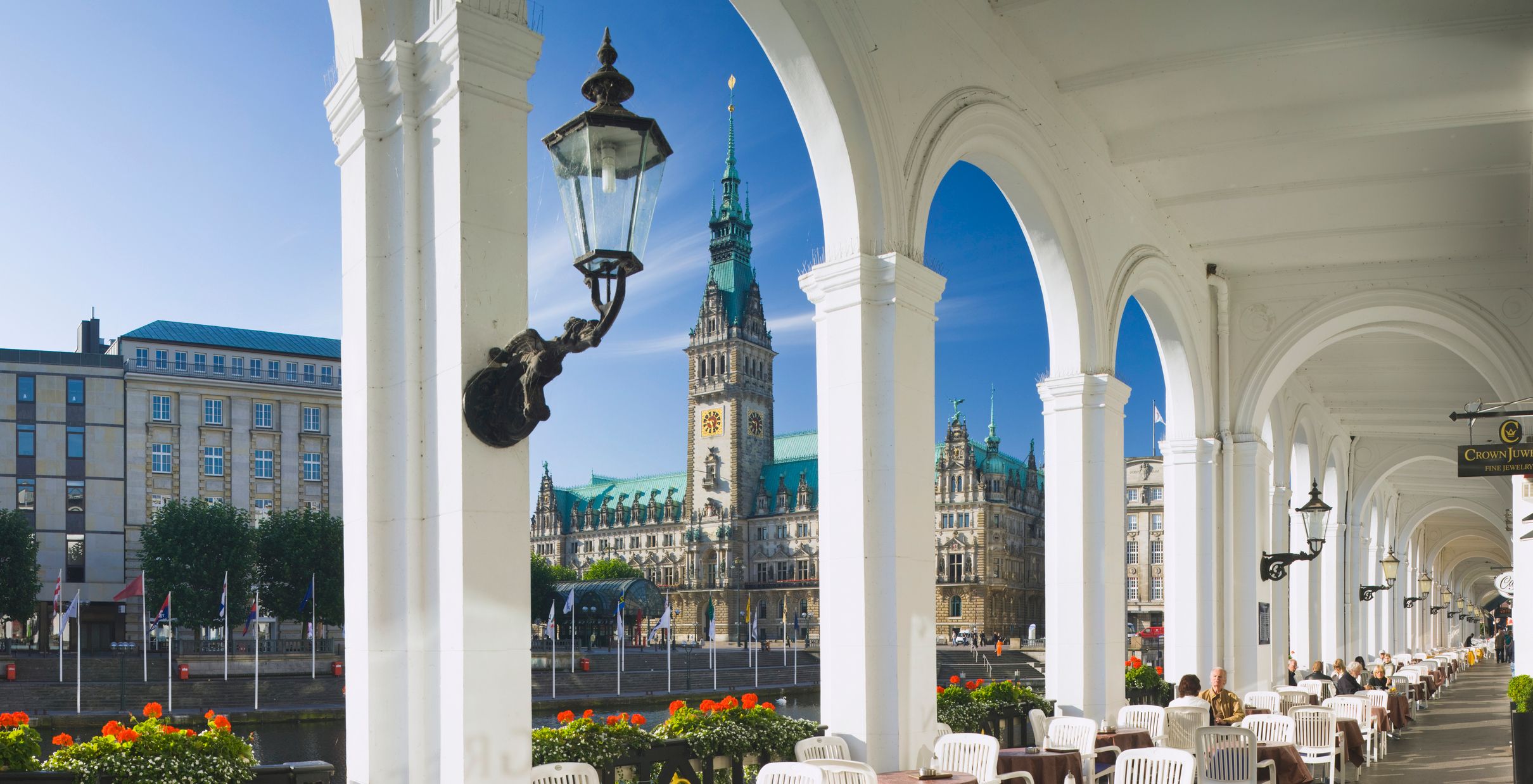 Blick auf das Hamburger Rathaus durch einen weißen Bogengang mit Tischen und Stühlen