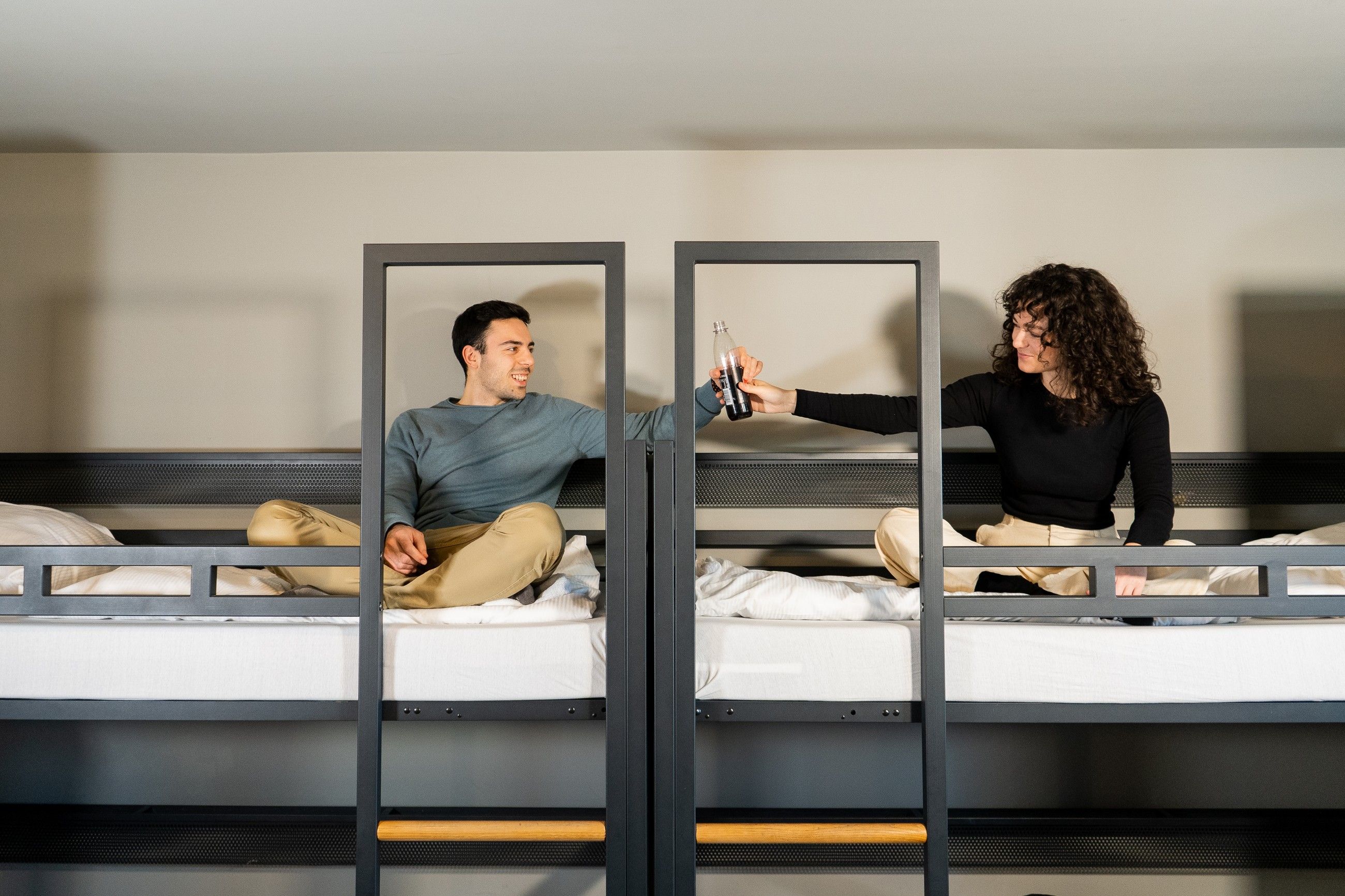 Zwei junge Erwachsene teilen sich ein Getränk in den Hochbetten eines Zimmers im a&o Hostel Berlin Hauptbahnhof