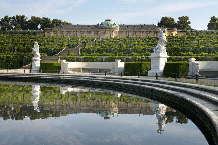 Brunnen mit Skulpturen herum, eine Treppe führt zum Schloss Sanssouci