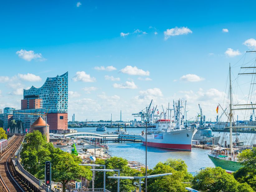 Hamburger Hafen mit Schiffen, einer Bahn und der Elbphilharmonie bei blauem Himmel