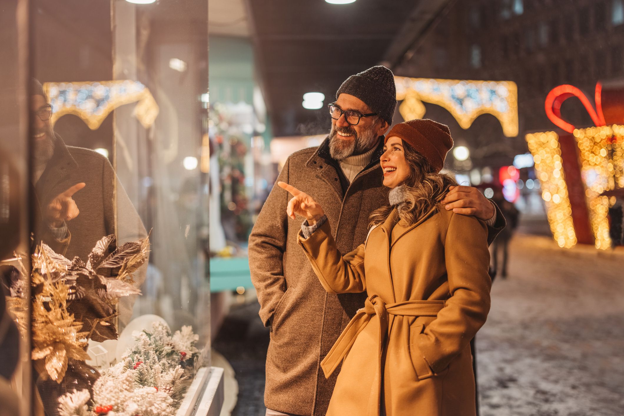 Ein warm eingepacktes Paar schaut sich ein leuchtendes Schaufenster an, im Hintergrund ist Weihnachtsdeko und Schnee