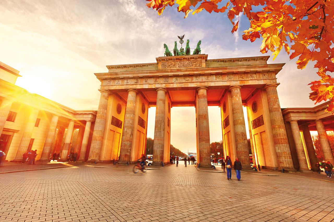 Brandenburger Tor in gold-orange gefärbtem Licht und herbstlich gefärbten Blättern eines Baumes