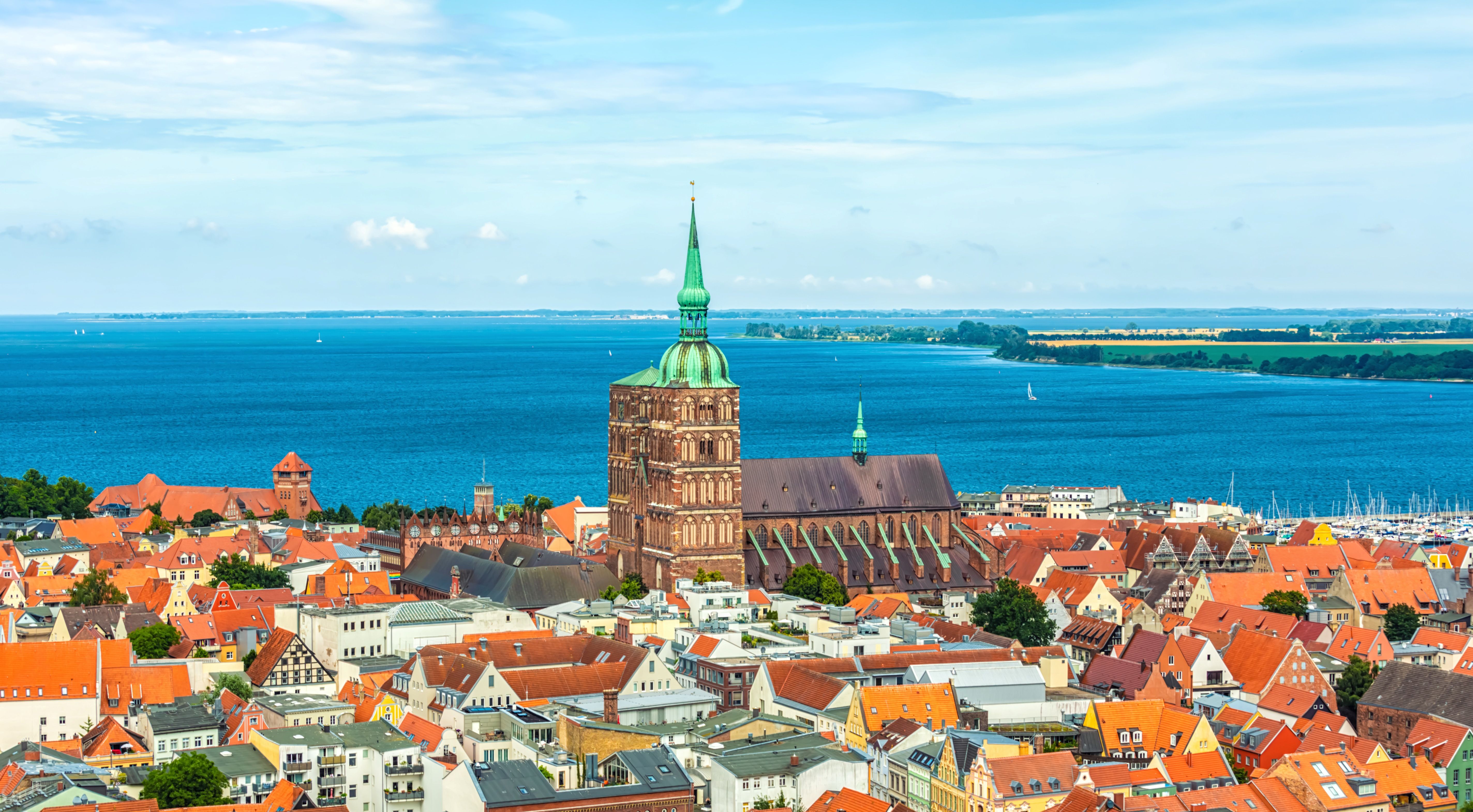Panoramablick auf die Altstadt von Stralsund mit markantem Kirchturm, roten Backsteindächern und der Ostsee im Hintergrund.