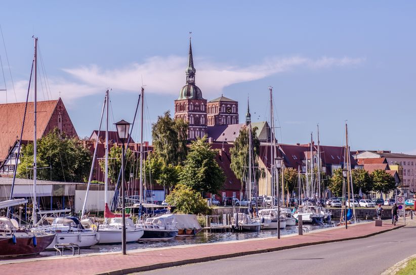 Segelboote liegen im Hafen von Stralsund vor historischer Kulisse mit Backsteingebäuden und Blick auf das ruhige Wasser der Ostsee.