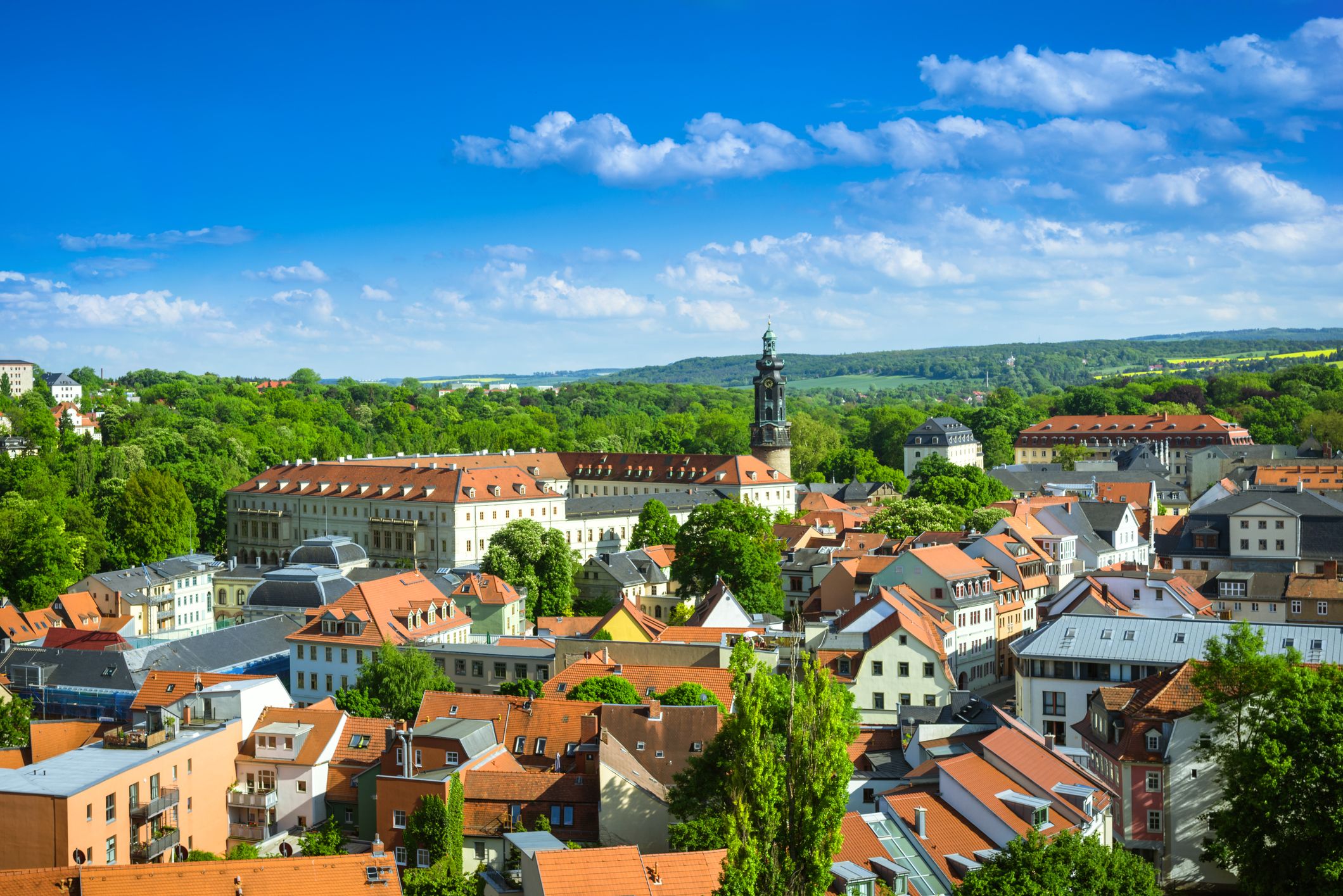Weitläufiges Panorama von Weimar mit Blick auf die historische Altstadt, markante Türme, grüne Parkanlagen und die umliegende Hügellandschaft unter offenem Himmel.