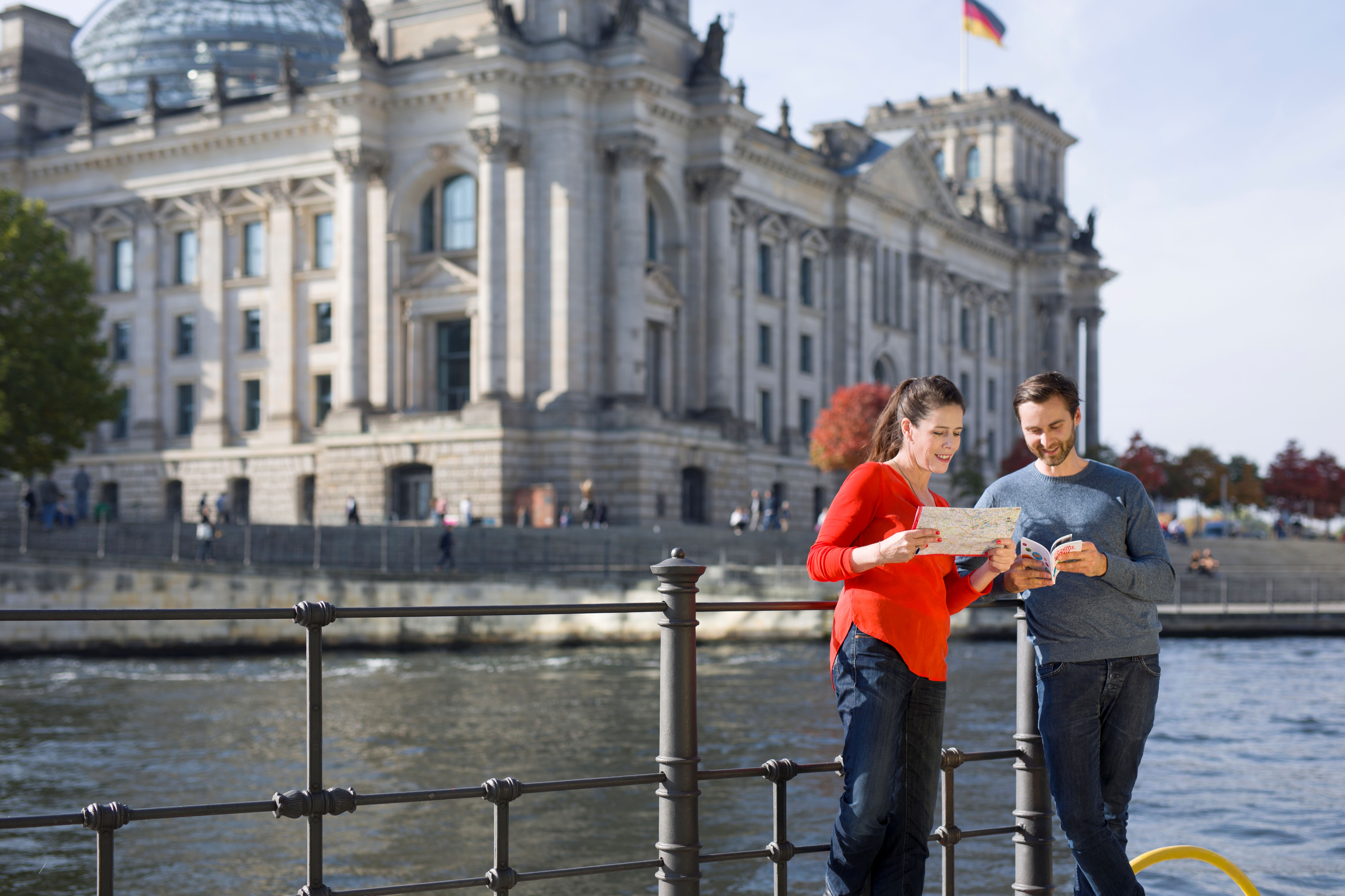 Paar schuat auf Karte und Rabattbuch und steht am Geländer vor der Spree und dem Reichstagsgebäude