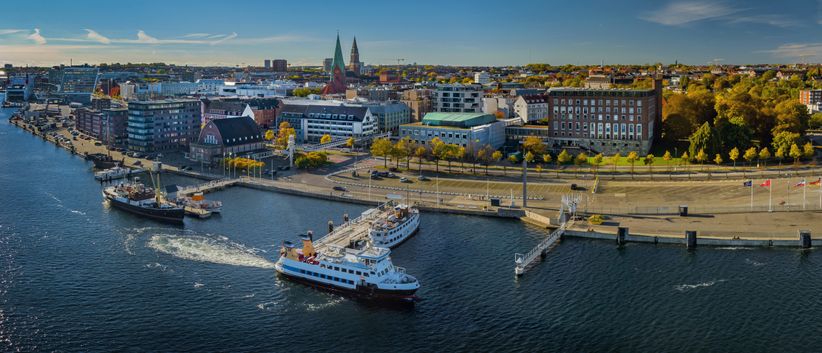 Luftaufnahme von Kiel mit Blick auf die Stadt, die Ostseeküste und ein an der Förde liegendes Kreuzfahrtschiff – maritimes Flair und Hafenatmosphäre aus der Vogelperspektive.