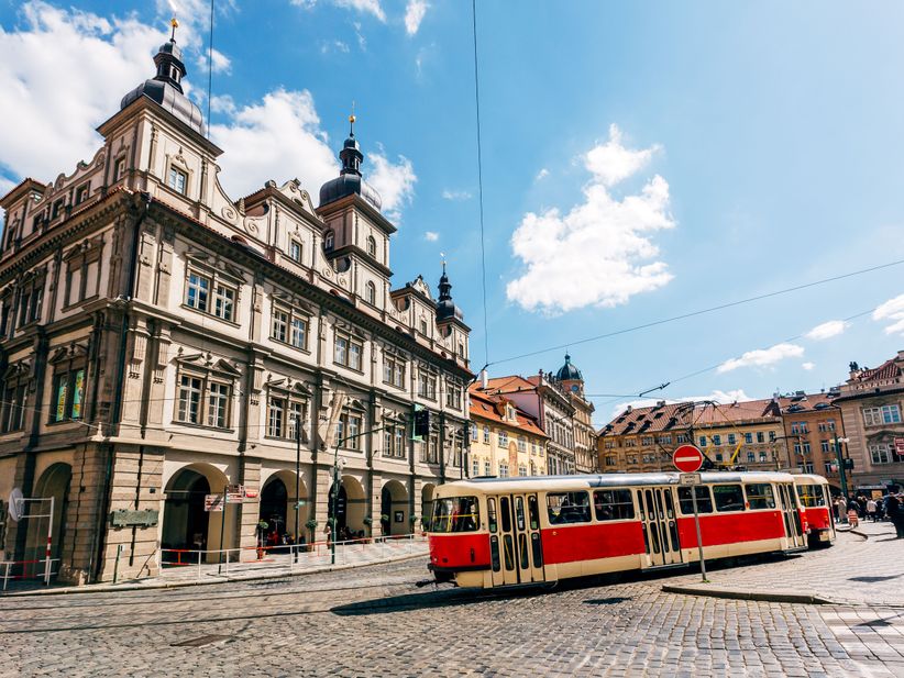 Rote Straßenbahn in Prag, fährt vor einer Kulisse aus historischen Gebäuden durch die Stadt.