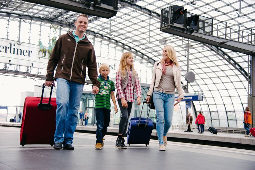 Familie mit zwei Kindern und Koffern gehen am Bahnhof zum Gleis