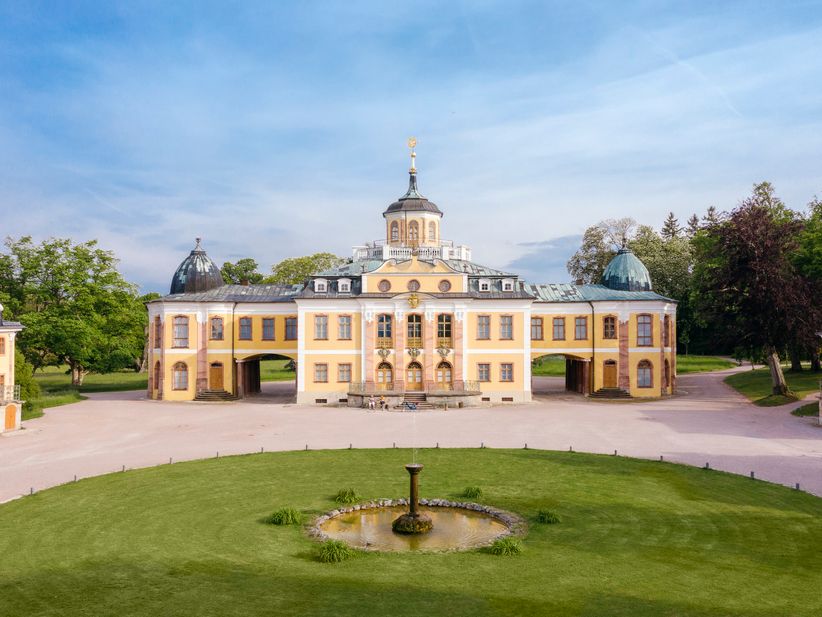 Frontale Ansicht des barocken Schlosses Belvedere bei Weimar mit seiner geschwungenen Fassade, verzierten Eingangspartie und vorgelagertem Ehrenhof, eingerahmt von symmetrisch angelegten Gartenflächen.