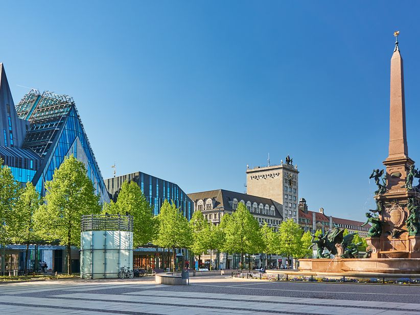 Brunnen auf dem Augustusplatz in Leipzig mit Bäumen vor umliegenden Gebäuden