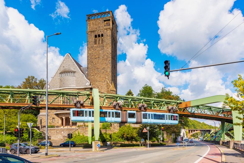 Schwebebahn über einer Kreuzung und vor einem steinernen Gebäude mit Turm in Wuppertal