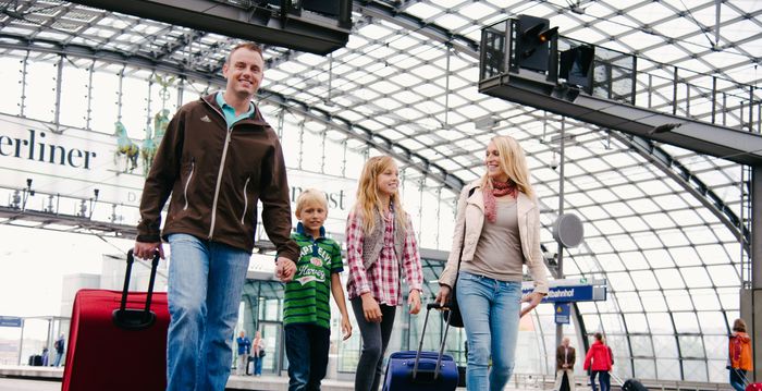 Familie mit zwei Kindern und Koffern gehen am Bahnhof zum Gleis