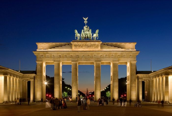 mehrere Menschen stehen vor dem beleuchteten Brandenburger Tor in Berlin bei Nacht