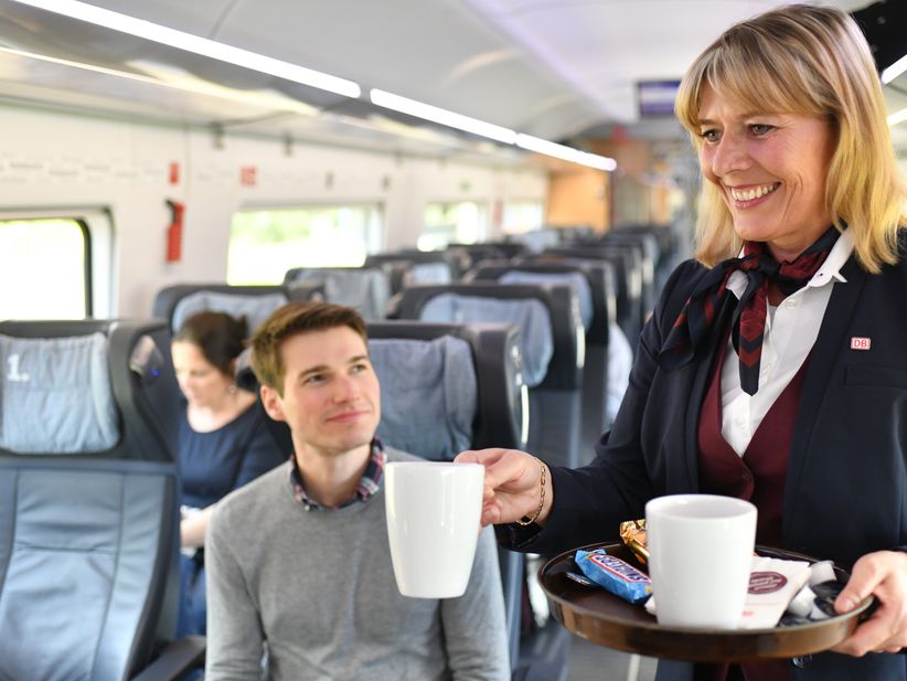 Servicepersonal im ICE Zug bringt Getränk an den Platz