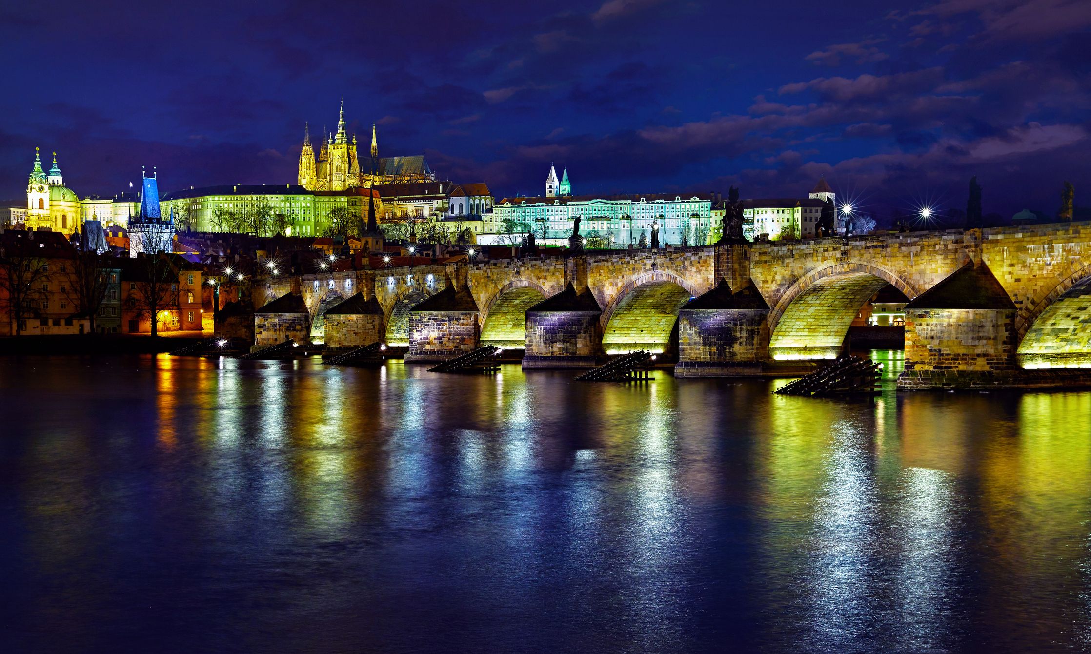Beleuchtete Karlsbrücke in Prag am Abend, die Lichter spiegeln sich in der Moldau.