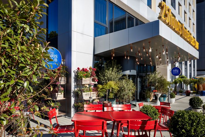Rote Stühle und Tische, viele Blumen und Pflanzen und Lichter an der Decke vom Eingang in das 25hours Tour Hotel