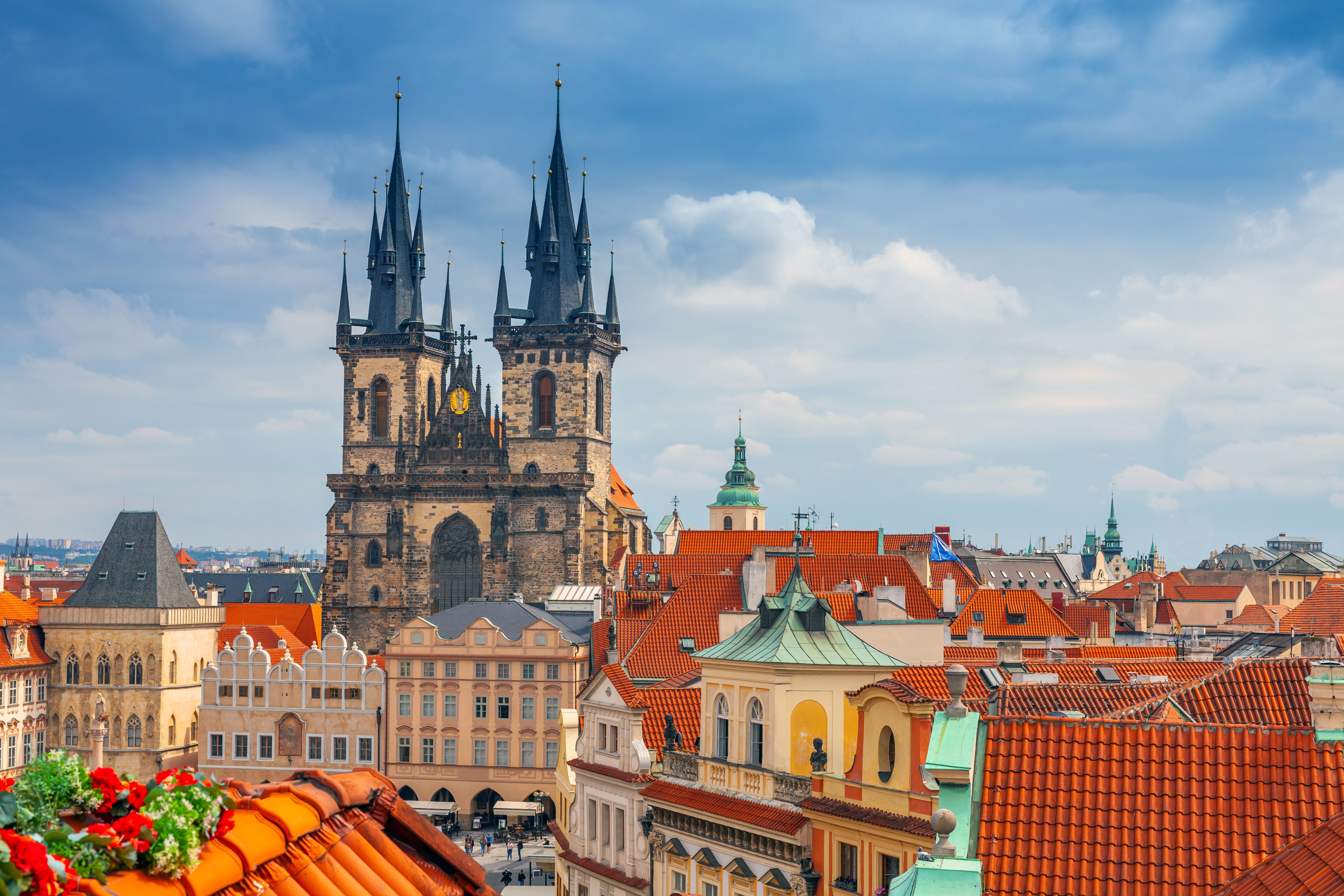 Blick auf die Teynkirche in Prag mit ihren markanten Türmen, darüber blauer Himmel und die Dächer der Altstadt.