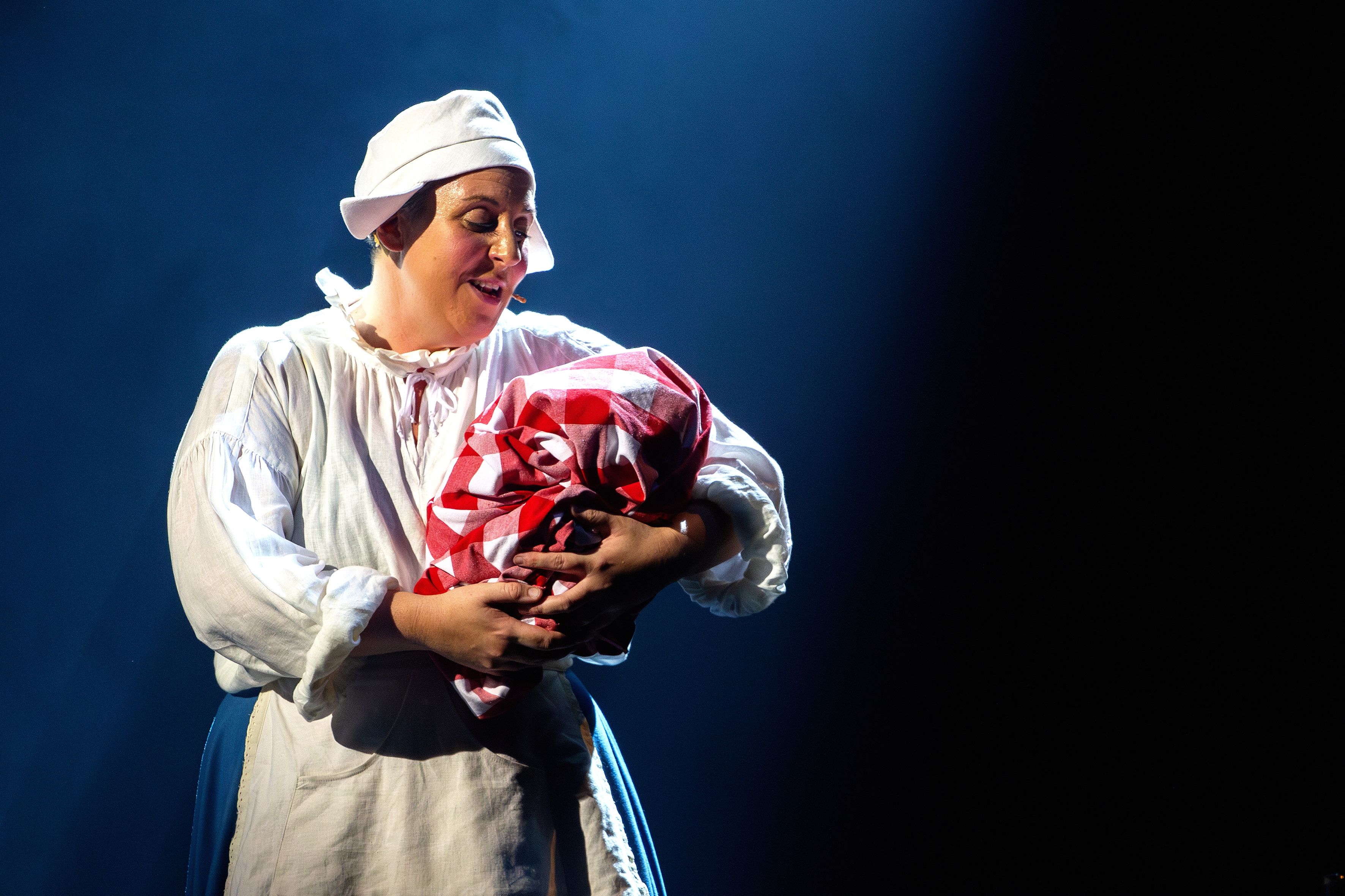 Darstellerin in der Rolle der Amme singt mit einem Bündel im Arm im Musical Die Amme
