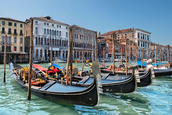 Mehrere kleine Boote liegen vertäut entlang einer Wasserstraße in Venedig, direkt vor einer historischen Häuserfront mit verwitterten Fassaden, Fensterläden und Balkonen. Die Szene zeigt den typisch venezianischen Alltag am Kanal.