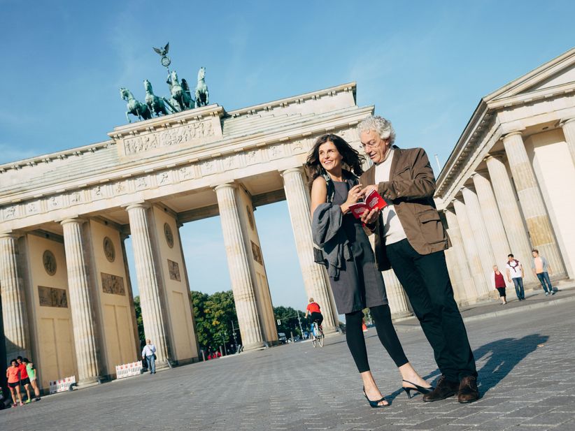 Ein älteres Paar steht vor dem Brandenburger Tor und schaut in das Rabattbuch der Berlin WelcomeCard