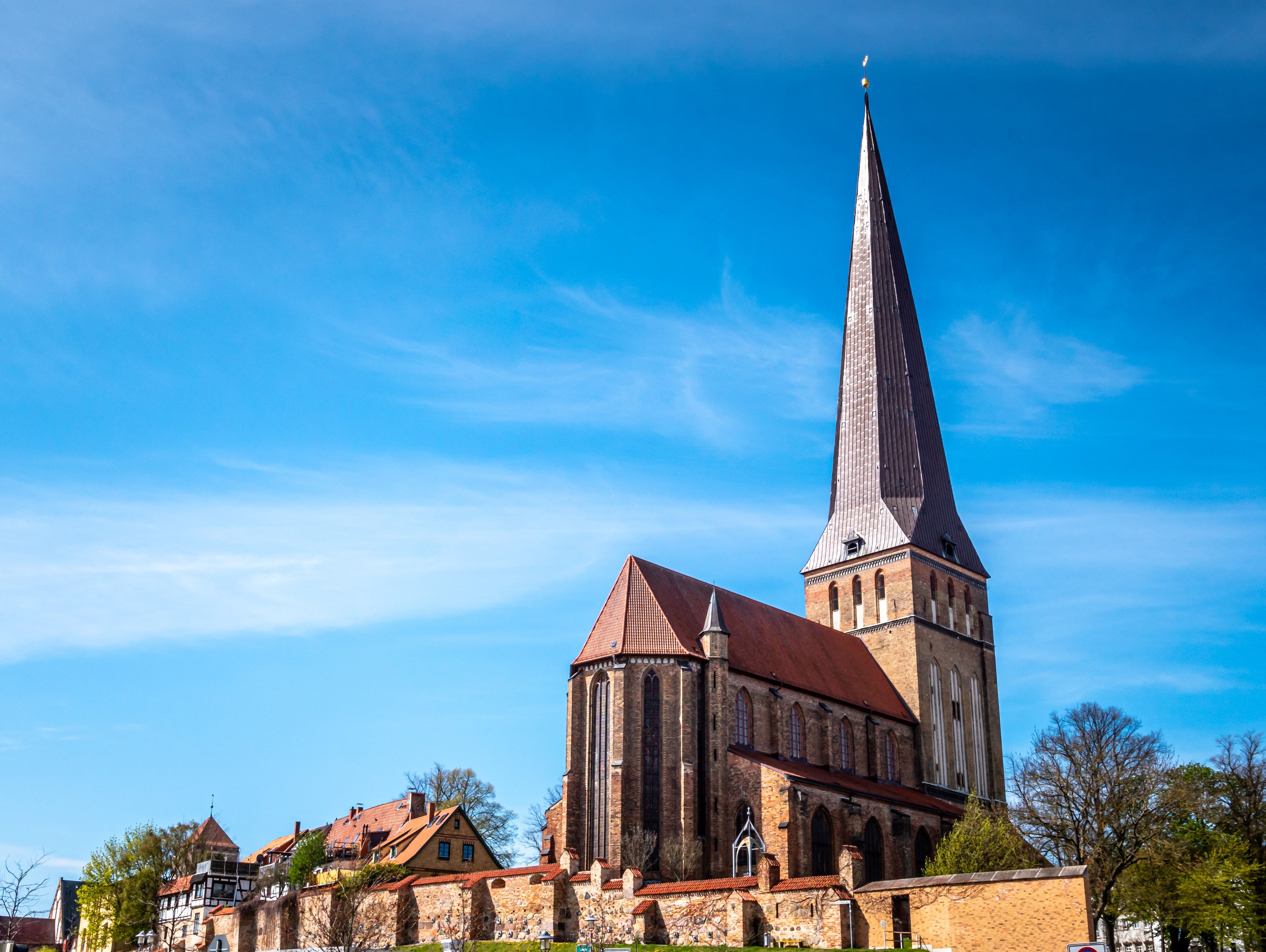 Außenansicht der Petrikirche in Rostock mit ihrem hohen, spitzen Turm vor blauem Himmel.