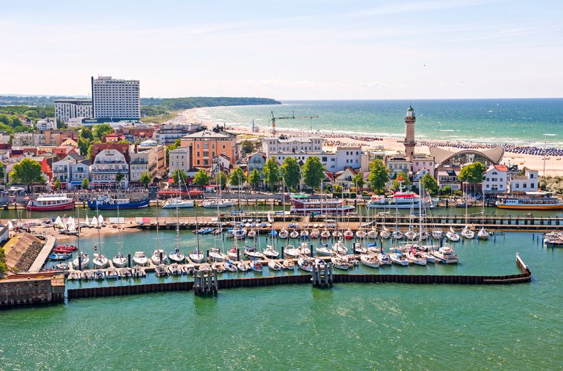 Luftaufnahme von Warnemünde mit breitem Sandstrand, der Mole, dem Leuchtturm und der Altstadt am Ufer der Ostsee.