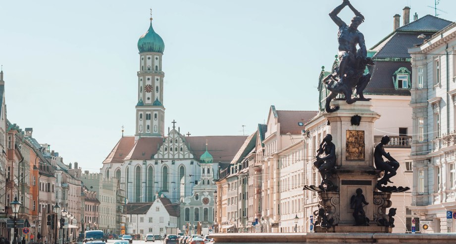 Der Augsburger Merkurbrunnen mit Blick auf die Basilika St. Ulrich und Afra - BAHNHIT.DE, © getty, Foto: taranchic