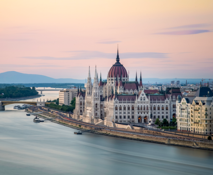 Parlamentsgebäude in Budpest bei rosa Himmel mit Donau davor