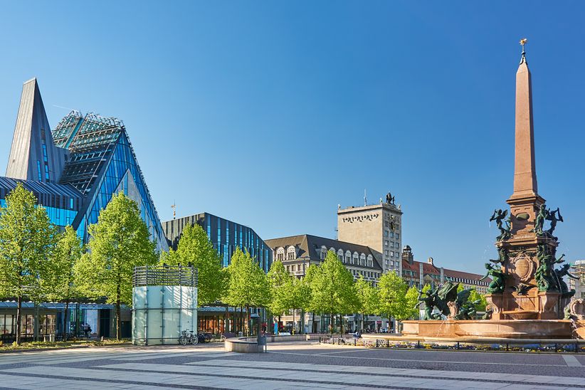 Brunnen auf dem Augustusplatz in Leipzig mit Bäumen vor umliegenden Gebäuden