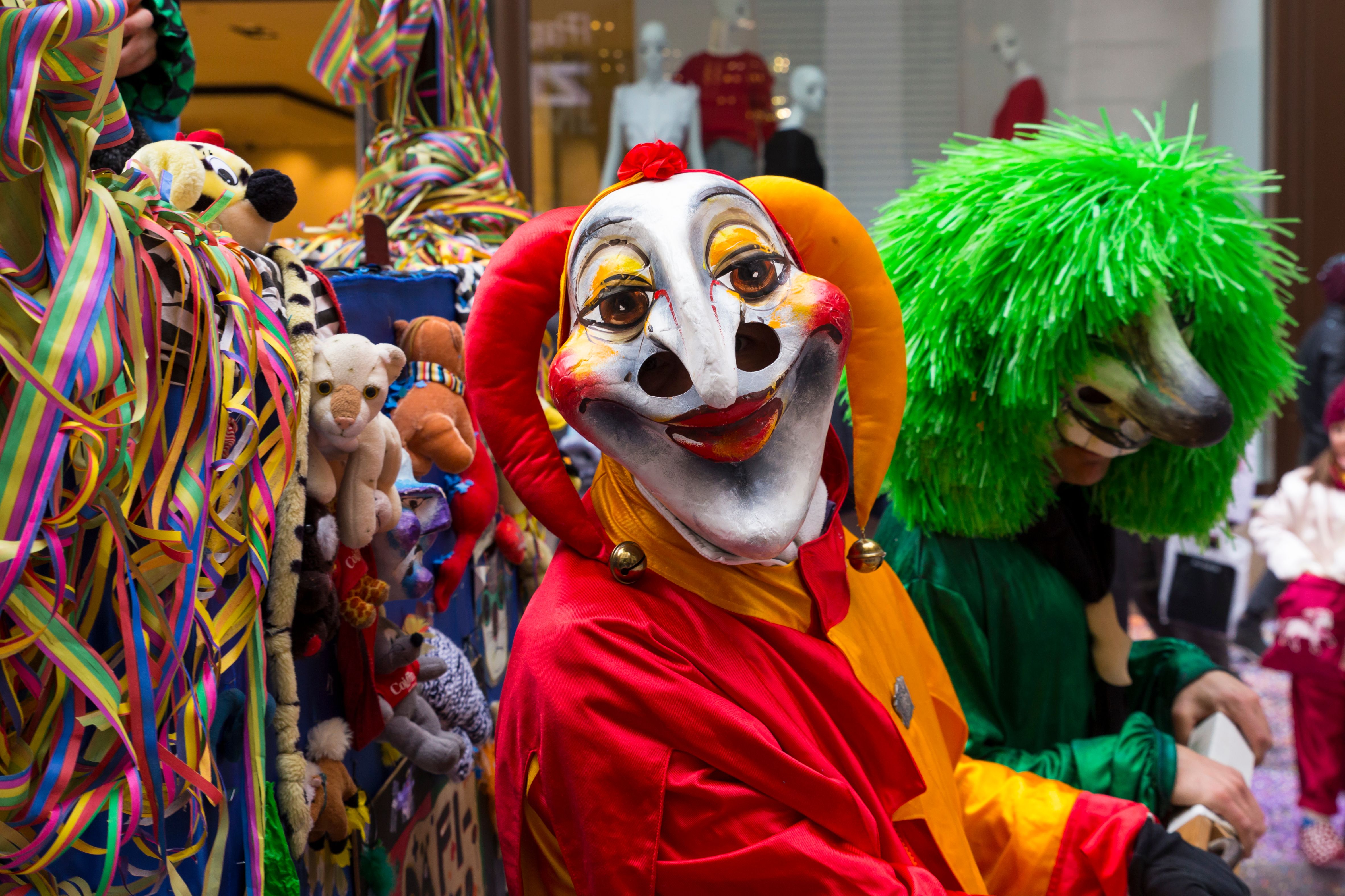 Zwei Menschen in bunten Clownskostümen mit großen Masken