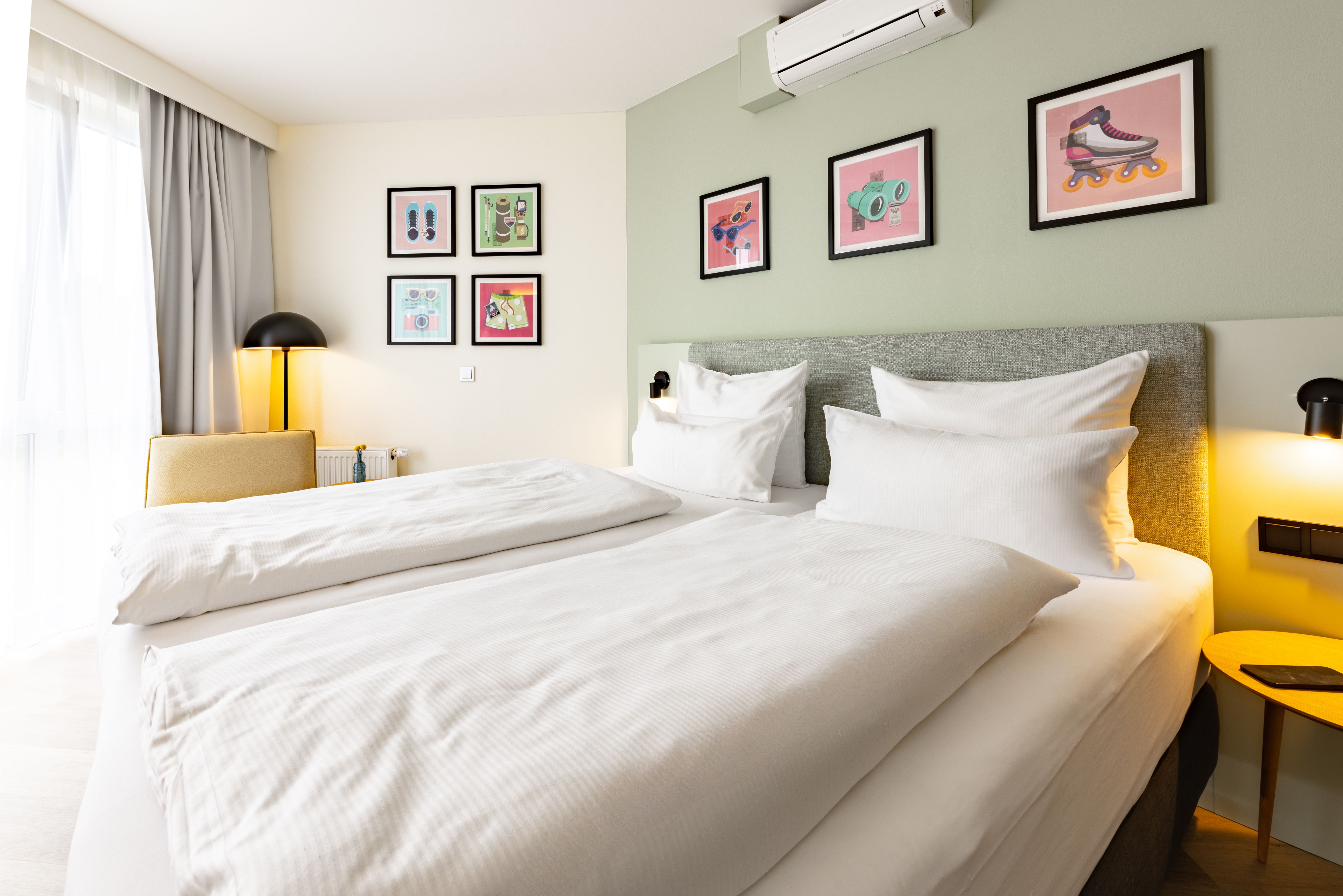 Ansicht eines Doppelzimmers inkl. Doppelbett türkisener Wand und farbigen Bilder.