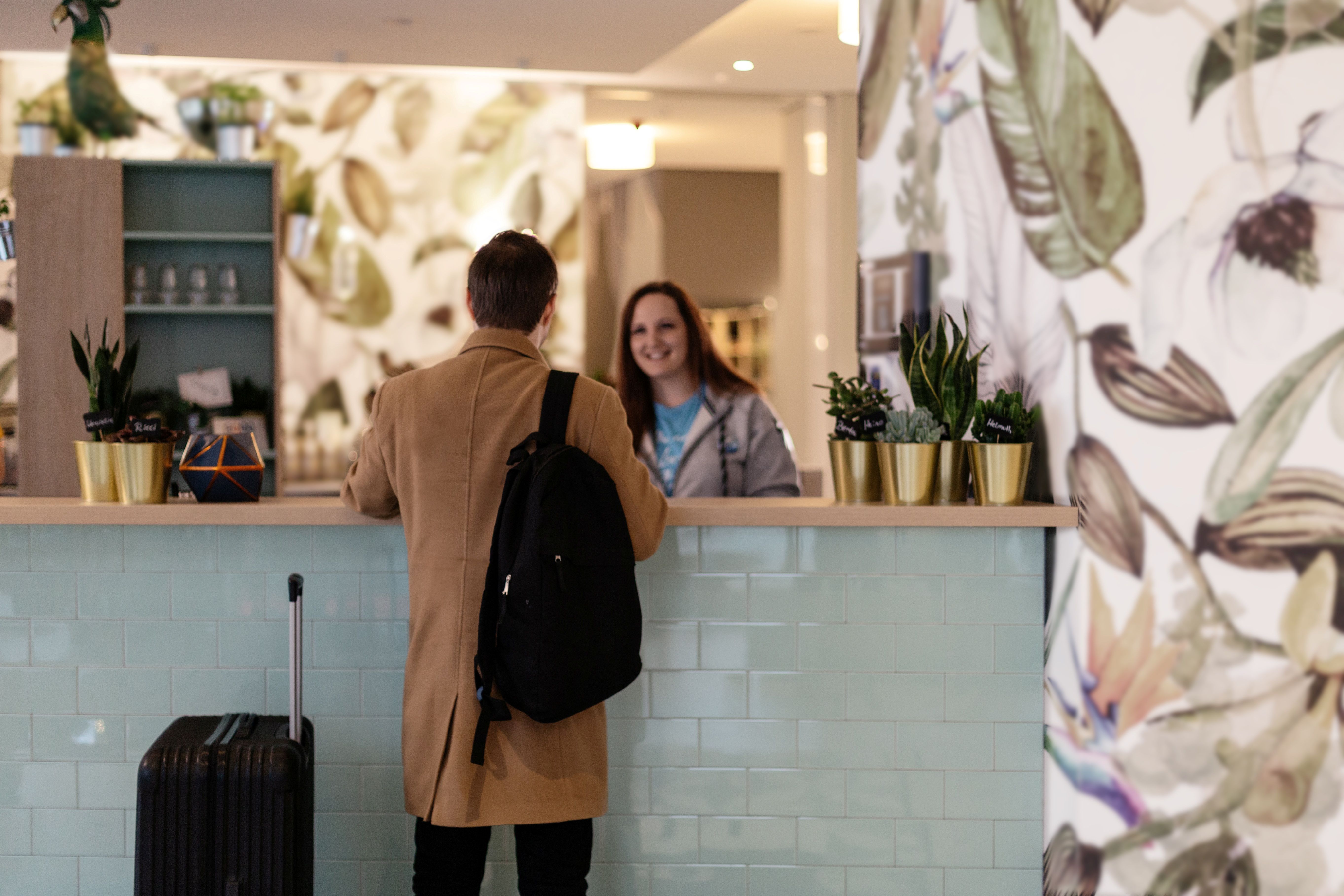 Moderne Hotelrezeption bei the niu: Eine freundliche Rezeptionistin begrüßt einen Gast mit Koffer beim Check-in in einem stylischen Lobby-Bereich mit markantem Design.