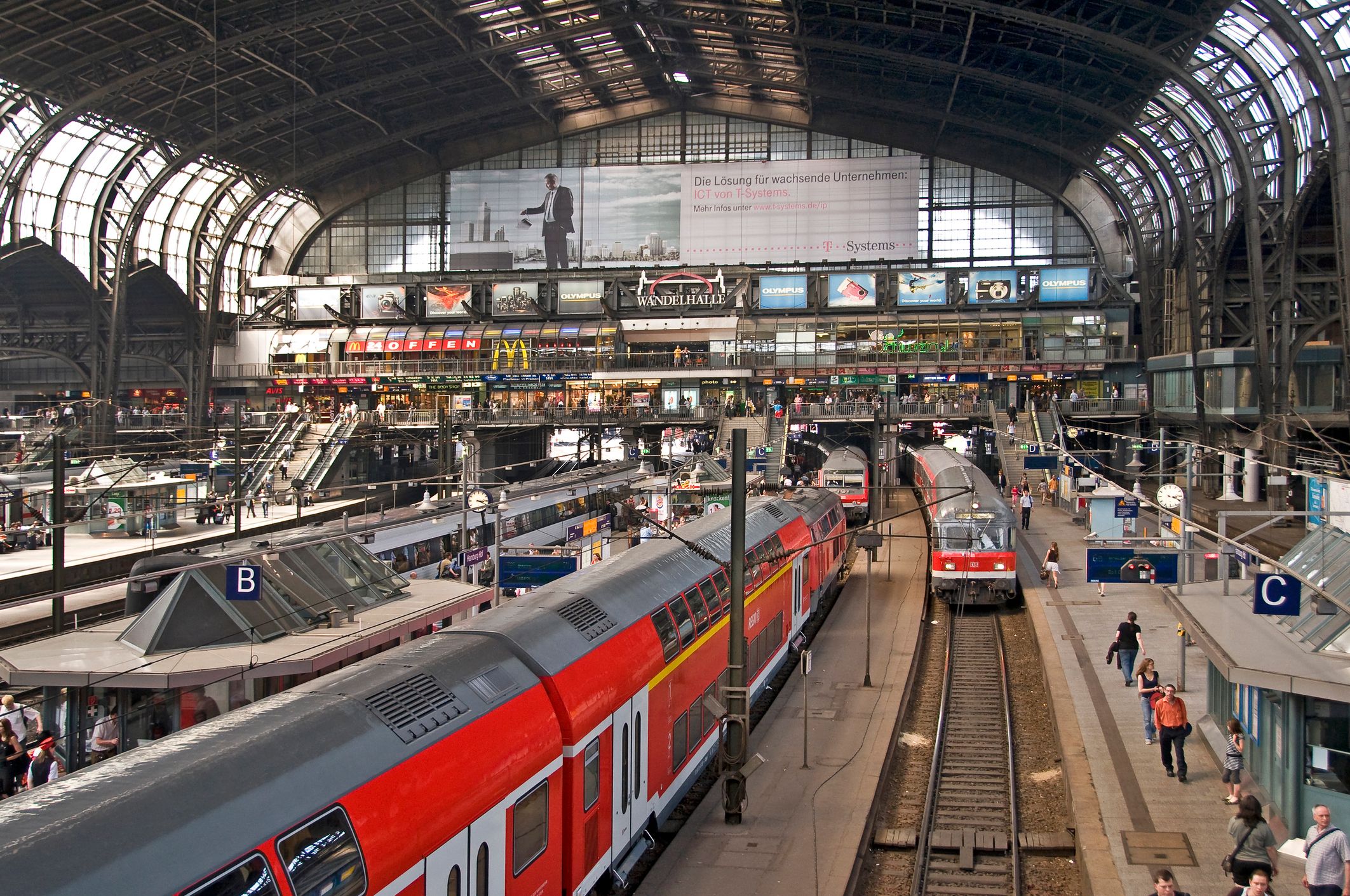 Blick von oben in die monumentale Bahnhofshalle des Hamburger Hauptbahnhofs auf die Gleisanlagen und einfahrende Züge unter der historischen Stahlkonstruktion.
