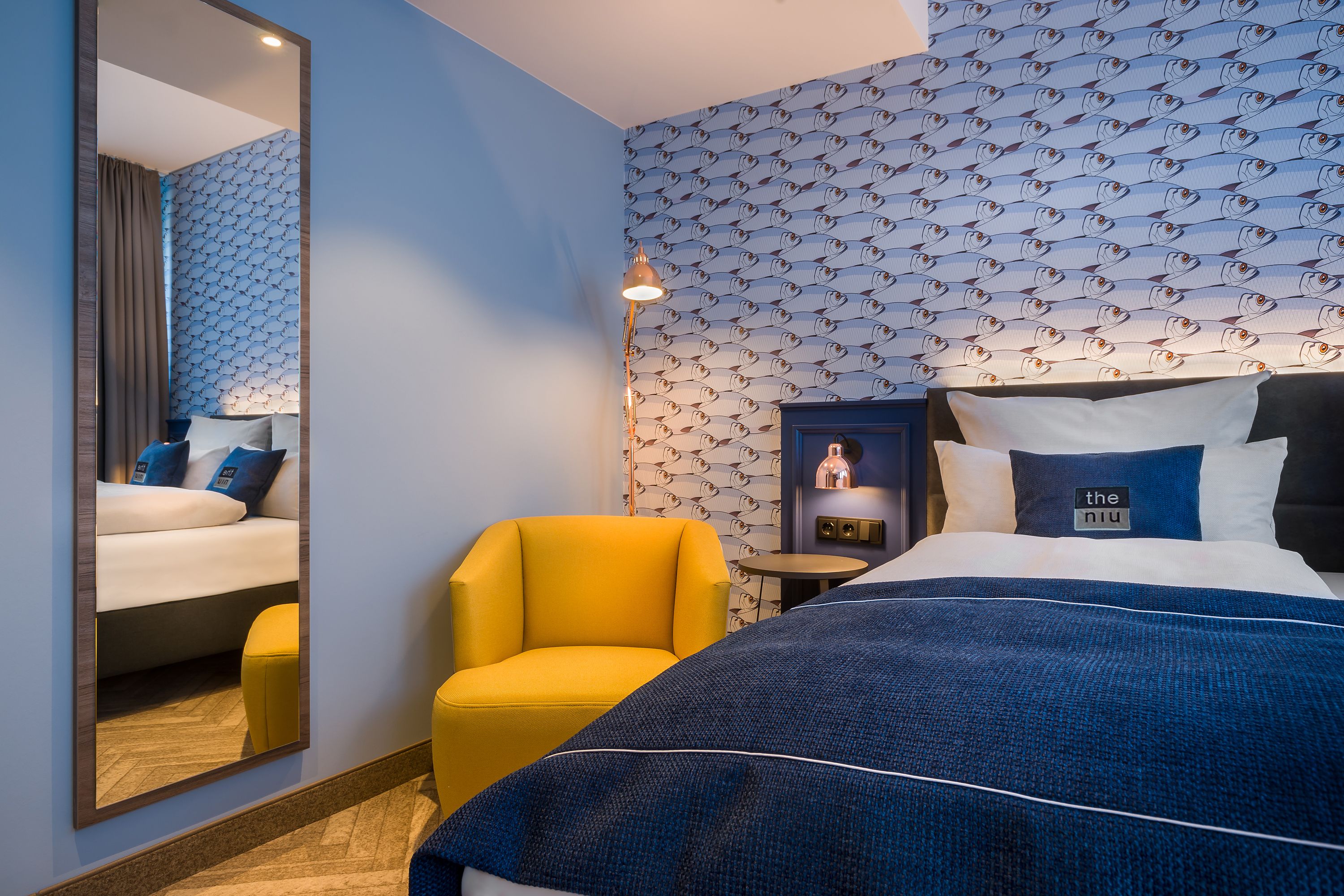 Modernes Doppelzimmer im Hotel the niu Welly Kiel mit hellen Holzmöbeln, maritimen Wandgrafiken und gelben Farbakzenten in skandinavischem Design.