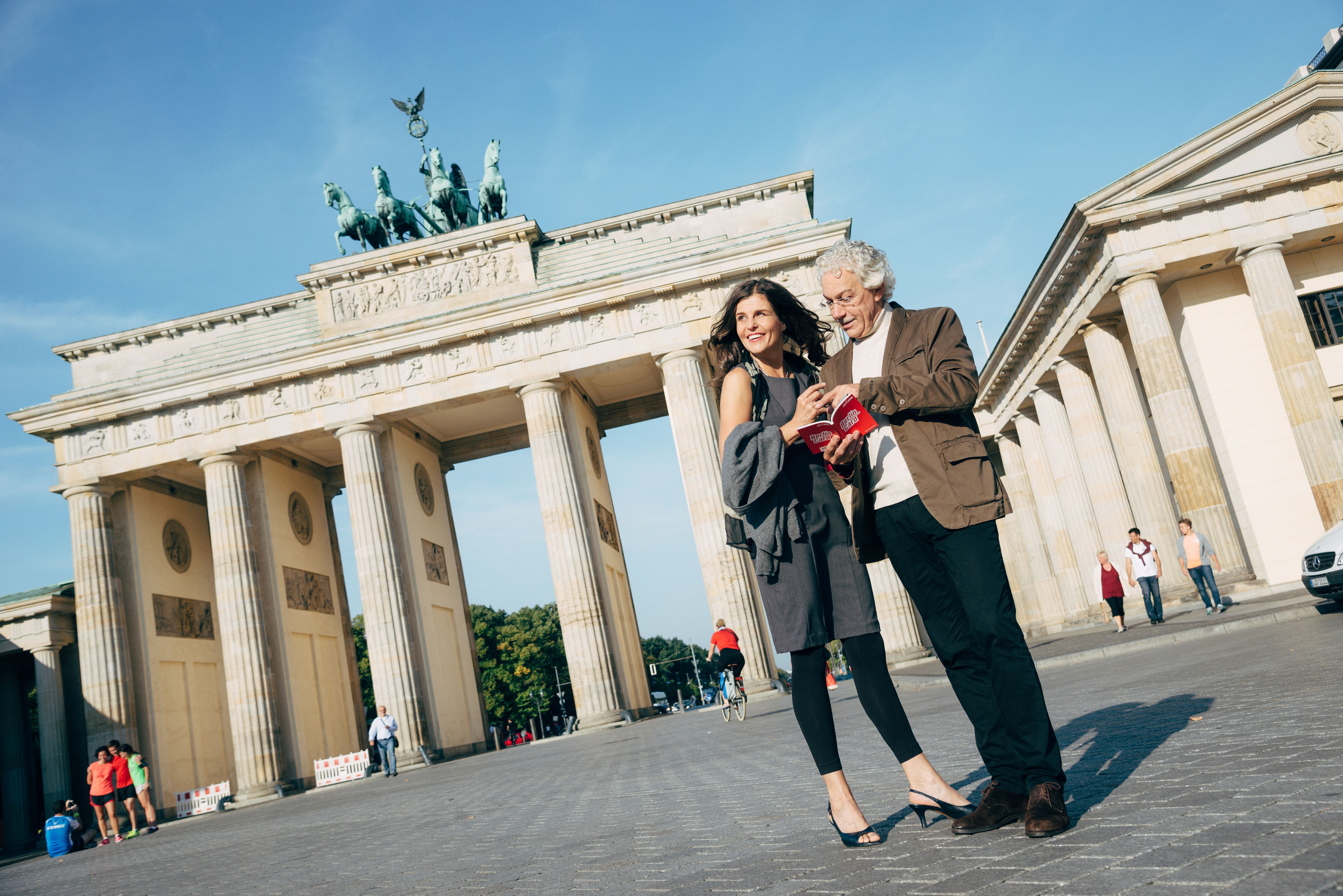 Ein älteres Paar steht vor dem Brandenburger Tor und schaut in das Rabattbuch der Berlin WelcomeCard