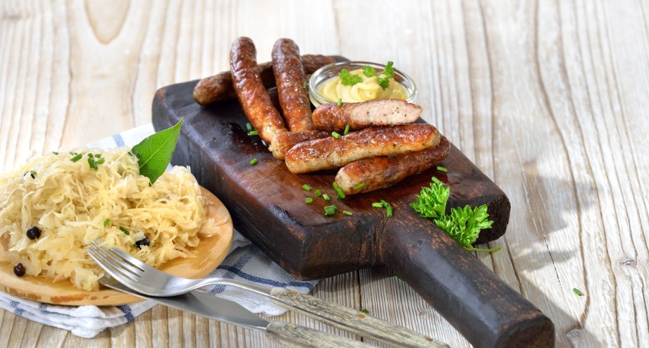 Traditionelles Gericht Nürnberger Bratwurst mit Sauerkraut auf einem Holzbrett serviert - BAHNHIT.DE, © getty, Foto: kabVisio