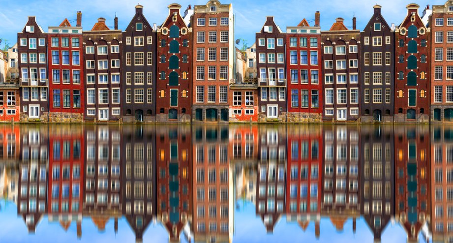 Aneinanderreihung traditioneller Häuser in Amsterdam und ihre Re­fle­xi­on im Wasser - BAHNHIT.DE, © getty, Foto: 2018 George Pachantouris