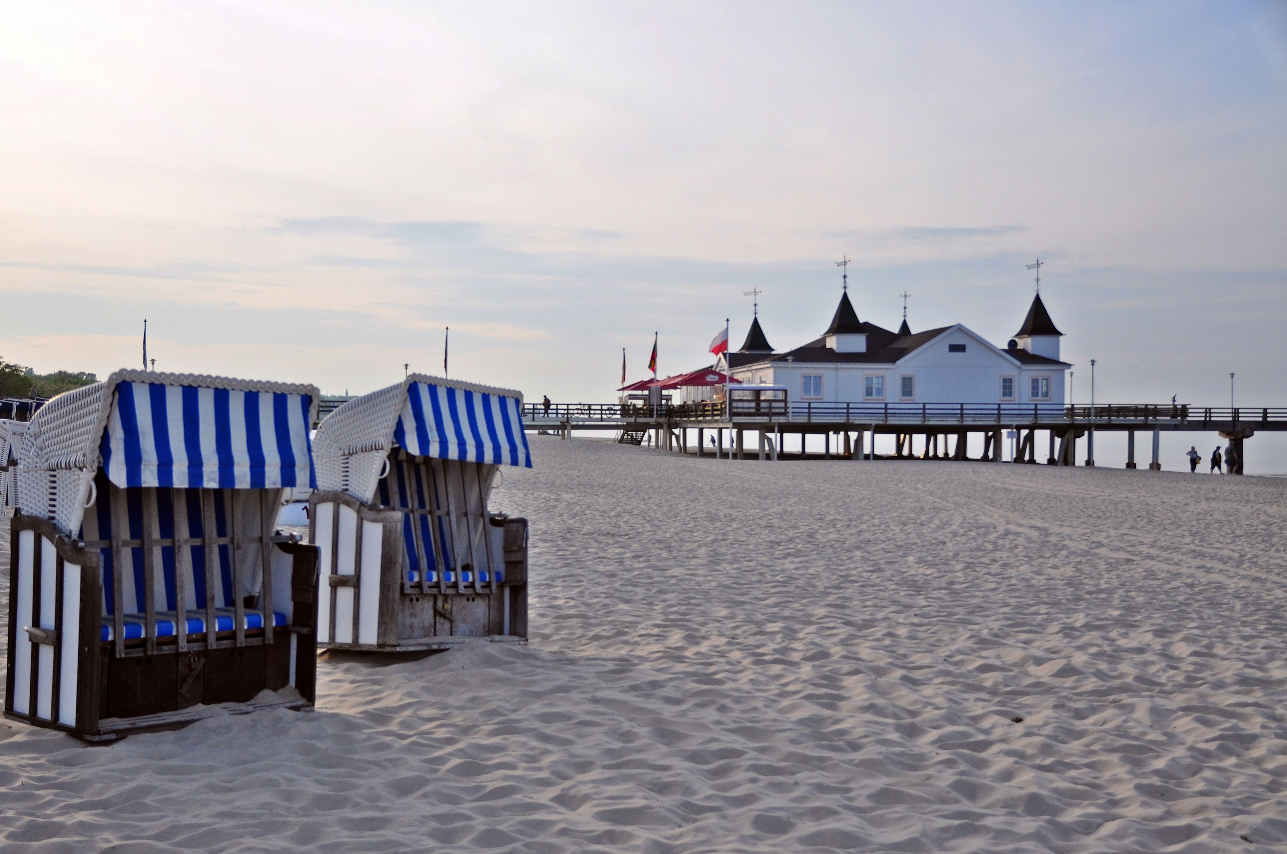 Blau-weiße Strandkörbe am Strand des Seebads Ahlbeck auf Usedom mit Blick auf die historische Seebrücke und die Ostsee.