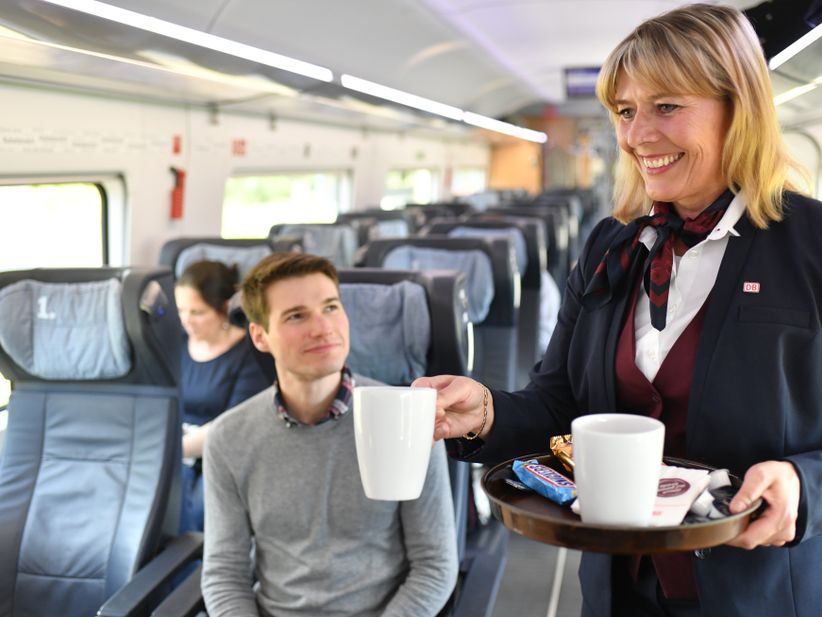 Servicepersonal im ICE Zug bringt Getränk an den Platz