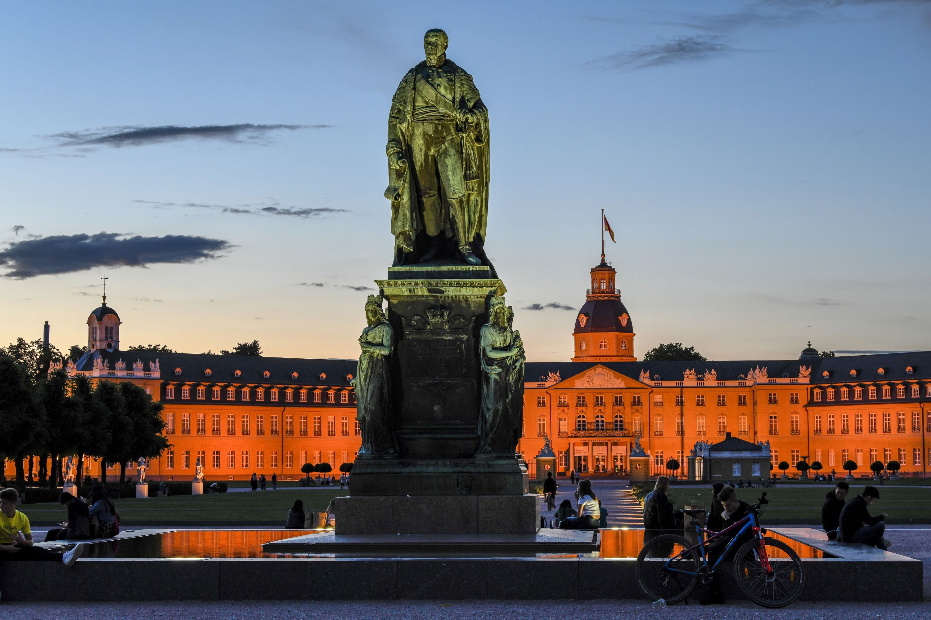 Beleuchtetes Schloss Karlsruhe in der Nacht mit Statue im Vordergrund