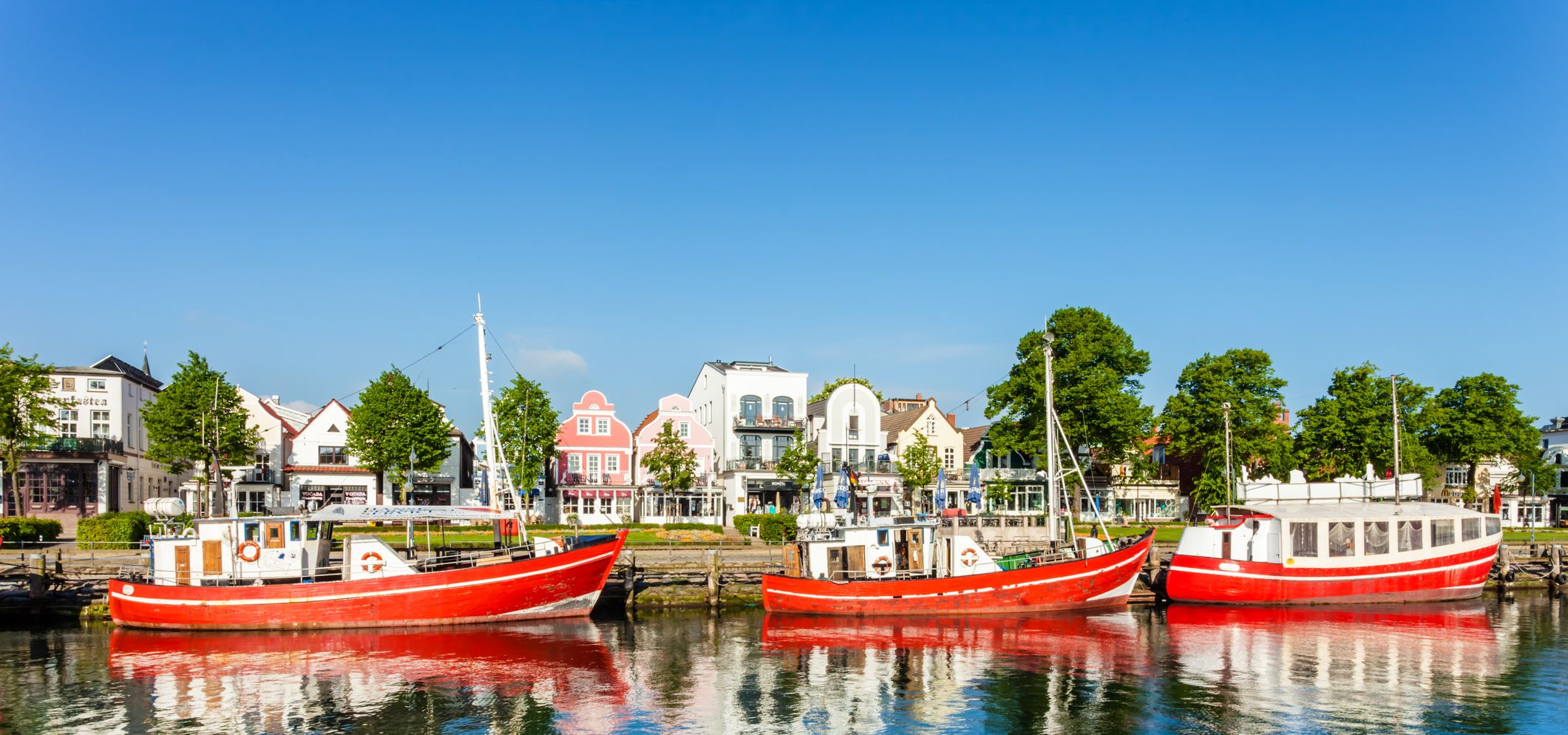 Warnemünde mit Booten im Alten Strom und Blick auf die historischen Häuser entlang der Uferpromenade.