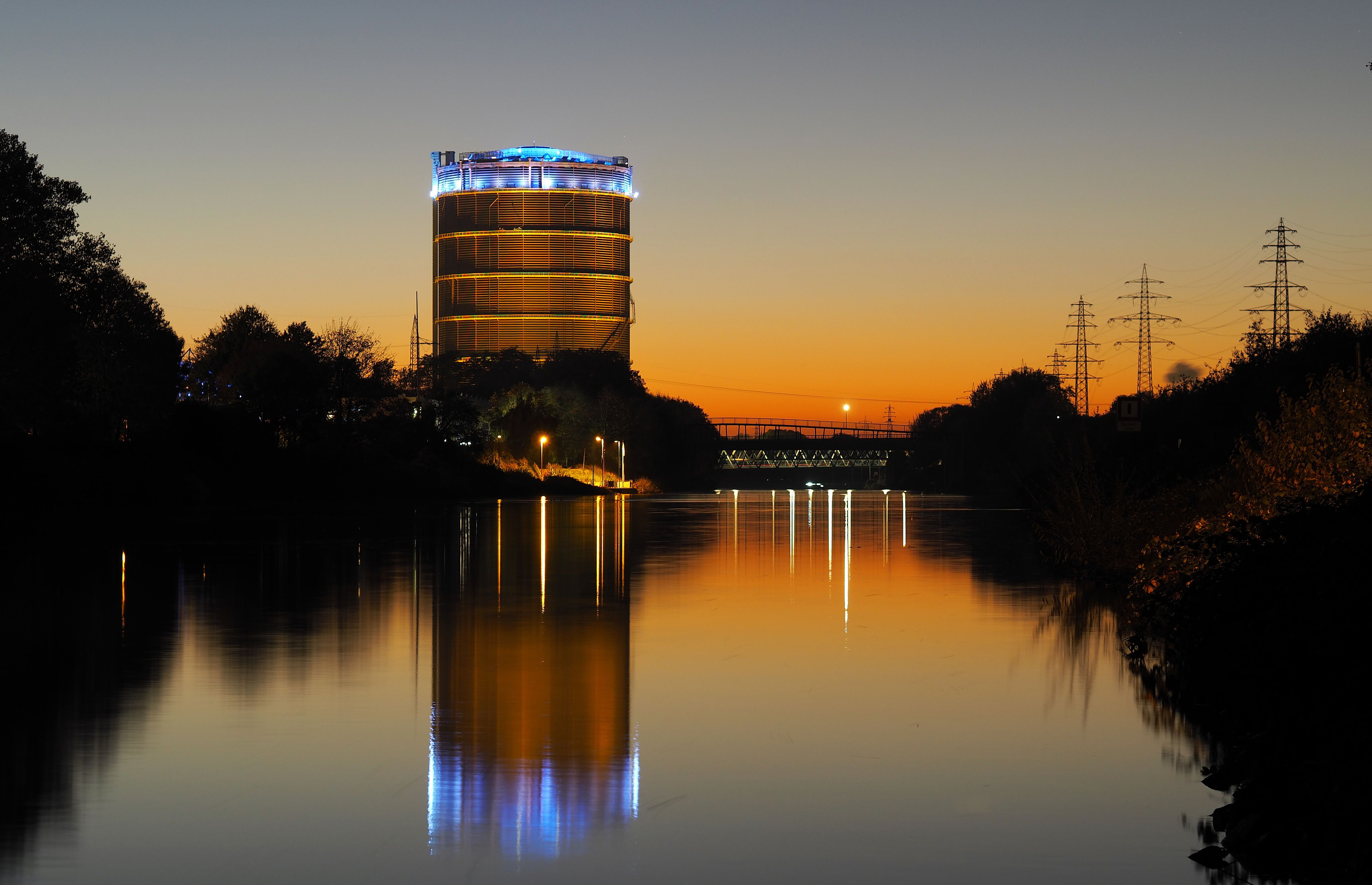 Beleuchteter Gasometer mit Spiegelung in Fluss in Oberhausen am Abend