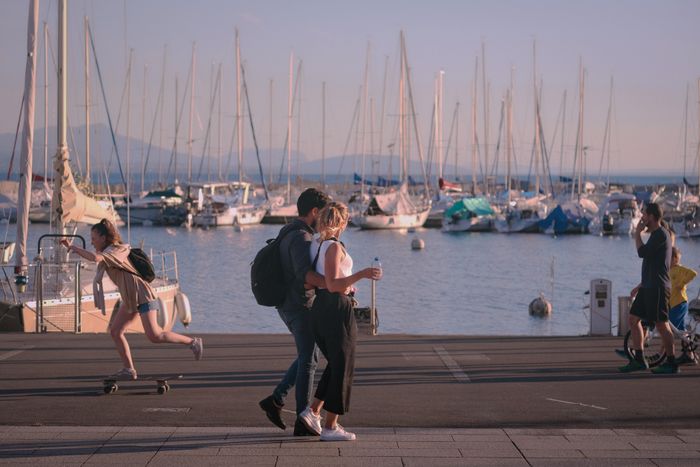 zwei Menschen spazieren an der Promenade des Genfer Sees in Lusanne entlang im Hintergrund sind mehrere Segelboote